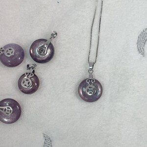 Puede incluir: Cinco colgantes circulares de color morado y plateado. Los colgantes est&aacute;n sobre una superficie blanca.