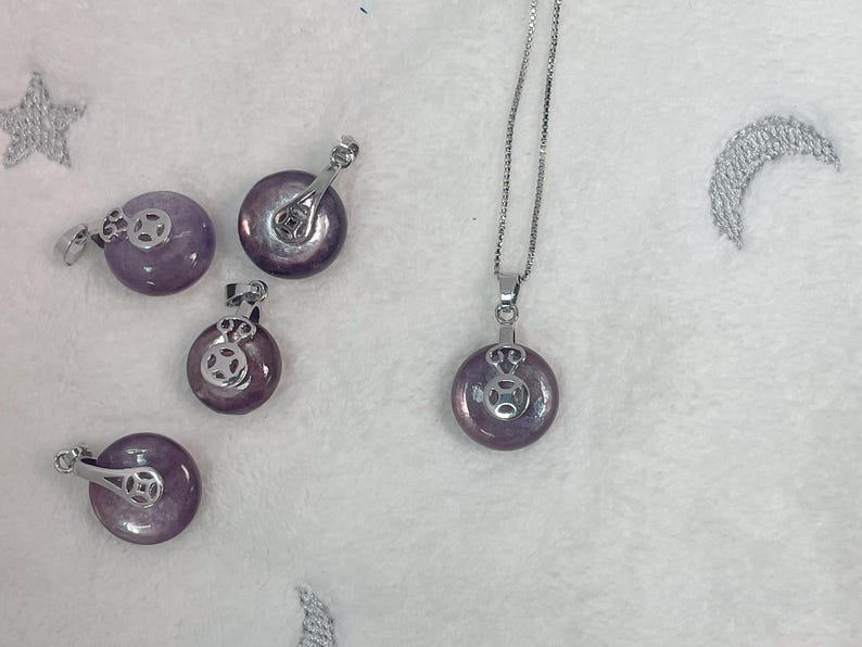 Puede incluir: Cinco colgantes circulares de color morado y plateado. Los colgantes est&aacute;n sobre una superficie blanca.
