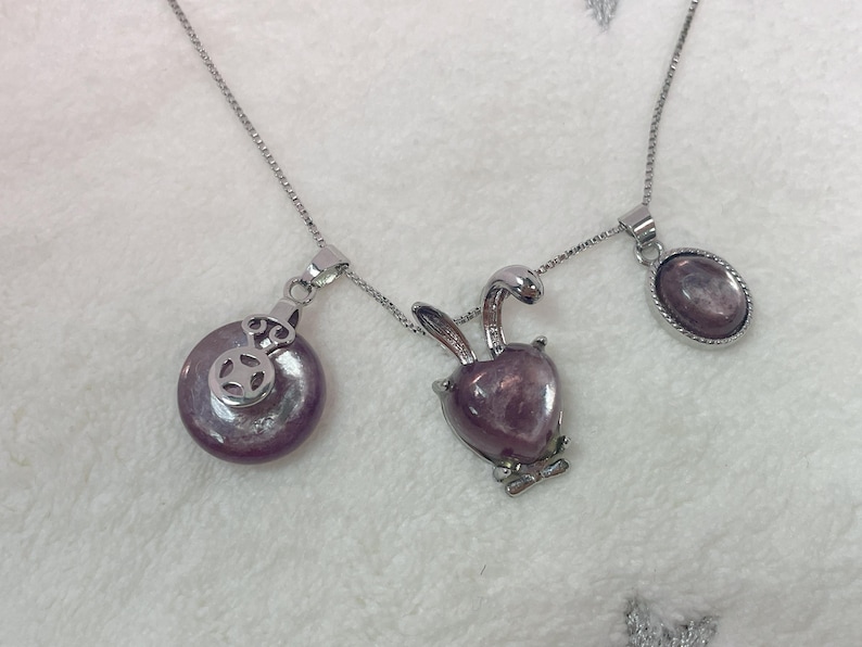 Puede incluir: Un collar de cadena de plata con tres colgantes. Los colgantes est&aacute;n hechos de piedra p&uacute;rpura y tienen diferentes formas, incluyendo un c&iacute;rculo, un coraz&oacute;n y un &oacute;valo.