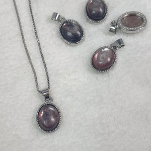 Puede incluir: Un collar de cadena de plata con un colgante ovalado de plata con una piedra iridiscente rosa y morada.