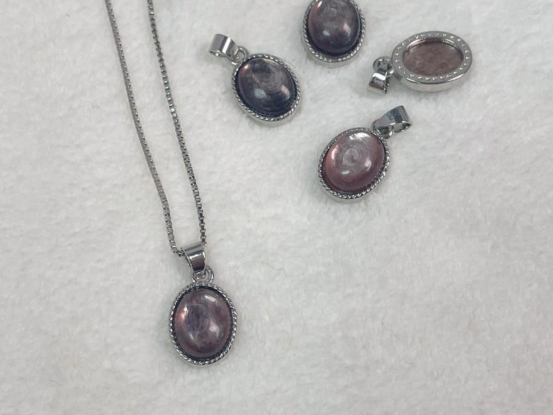 Puede incluir: Un collar de cadena de plata con un colgante ovalado de plata con una piedra iridiscente rosa y morada.