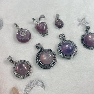 Puede incluir: Una colecci&oacute;n de ocho colgantes de plata con detalles de piedras preciosas p&uacute;rpuras y rosas. Los colgantes presentan varios dise&ntilde;os, incluyendo un conejo, una flor y formas geom&eacute;tricas.