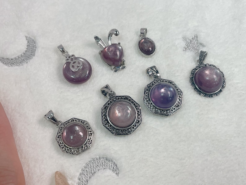 Puede incluir: Una colecci&oacute;n de ocho colgantes de plata con detalles de piedras preciosas p&uacute;rpuras y rosas. Los colgantes presentan varios dise&ntilde;os, incluyendo un conejo, una flor y formas geom&eacute;tricas.