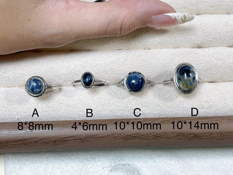 May include: Four silver rings labeled A, B, C, and D, each featuring a blue and black patterned stone. Ring A is 8x8mm, B is 4x6mm, C is 10x10mm, and D is 10x14mm. The rings are arranged in a row on a soft, light-colored display surface.