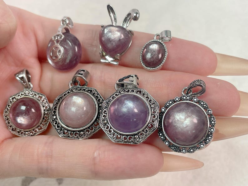 Puede incluir: Siete colgantes de plata con piedras moradas e iridiscentes. Los colgantes son de varias formas, incluyendo redonda, ovalada y un conejo.
