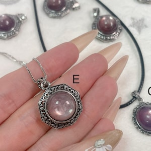 Puede incluir: Tres collares de plata con diferentes estilos de colgantes. Cada colgante presenta una piedra preciosa redonda e iridiscente en tonos de rosa y morado. Los colgantes est&aacute;n rodeados de intrincados dise&ntilde;os de plata. Los collares est&aacute;n etiquetados con las letras E y G.