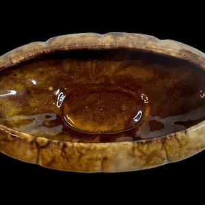 May include: A brown ceramic planter with a wavy rim and a glossy finish. The planter is oval shaped and has a slightly raised center.
