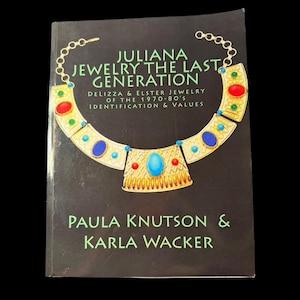 May include: A book titled "Juliana Jewelry The Last Generation" with a black cover. The cover features a gold necklace illustration with red, blue, and green accents. The authors' names, Paula Knutson & Karla Wacker, are printed below the necklace image.