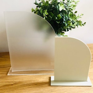 May include: Two acrylic display stands with rounded edges. The larger stand is frosted and the smaller stand is white.