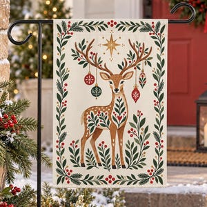 May include: A rectangular garden flag featuring a central illustration of a deer with antlers adorned with hanging Christmas ornaments. The deer is surrounded by a decorative border of green pine branches and red berries on a cream background.