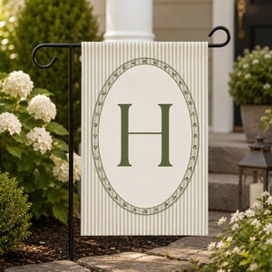 Peut inclure: Un drapeau de jardin rectangulaire avec un motif à rayures verticales beige clair et blanc. Au centre, une grande lettre H vert foncé est entourée d'un cadre ovale orné d'un petit motif de vigne florale verte.