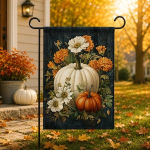 Puede incluir: Una bandera de jardín rectangular con un fondo de grano de madera azul oscuro, una calabaza blanca grande y una calabaza naranja más pequeña rodeadas de flores blancas y naranjas y hojas verdes, colgada en un soporte de metal negro.