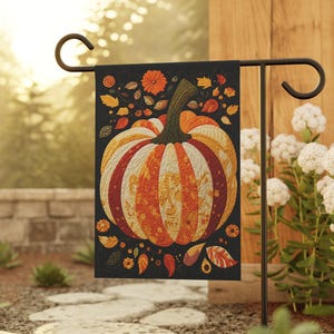 Puede incluir: Una bandera de jardín rectangular que presenta una gran ilustración central de una calabaza sobre un fondo negro. La calabaza está compuesta por segmentos verticales en tonos naranja, amarillo y rojo, decorados con intrincados motivos florales.