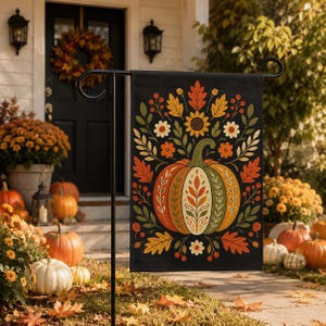 May include: A rectangular garden flag featuring a black background with a central orange and green pumpkin illustration. The pumpkin is surrounded by a symmetrical arrangement of autumn leaves, berries, and flowers in shades of yellow, orange, and red.