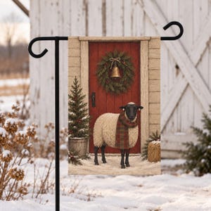 May include: A rectangular garden flag featuring a sheep with black fur on its head and legs, wearing a red and green plaid scarf. The sheep stands before a red door with a green wreath and a gold bell, flanked by a small potted evergreen tree.
