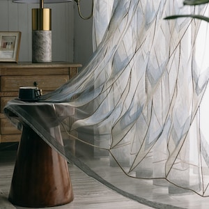May include: A sheer white curtain with a geometric pattern in shades of blue and brown. The curtain is flowing in the wind, creating a soft and elegant look.