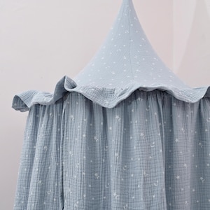 May include: A light blue canopy with a star and moon pattern. The canopy has a ruffled edge and a conical top. The fabric appears to be a soft, textured material. The canopy is designed to hang from the ceiling.