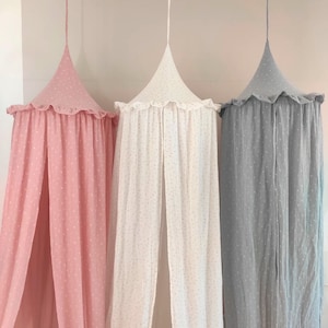 May include: Three canopy bed curtains in pink, white, and gray with a dotted pattern. The curtains have a ruffled edge and are made of a lightweight fabric.