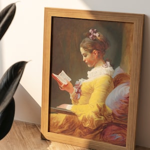 May include: A framed painting of a young woman in a yellow dress reading a book. The painting is set in a room with a soft, warm light. The woman's hair is pulled back and she is wearing a white collar. The painting is framed in a simple wooden frame.