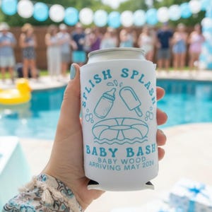 May include: A white can cooler with the text "Splish Splash Baby Bash" in blue, featuring illustrations of a baby bottle, popsicle, and a life preserver. The text "Baby Wood Arriving May 2024" is also included. The background shows a pool and party decorations.
