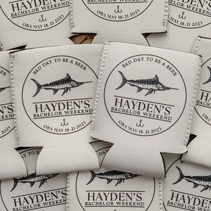 May include: A set of eight beige can coolers with a black marlin fish graphic and the text "Hayden's Bachelor Weekend" with a fishing hook symbol and the date "OBA May 18-21 2023".