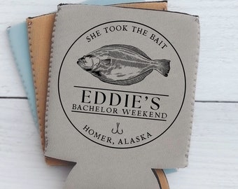 Op de afbeelding: Grijze koelbox voor blikjes met een zwart cirkelvormig ontwerp met een vis, de tekst "She took the bait", "Eddie's Bachelor Weekend" en "Homer, Alaska".