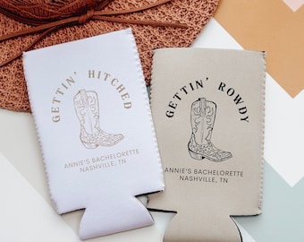 Puede incluir: Dos enfriadores de latas blancos y beige con diseños de botas de vaquero. Uno dice "GETTIN' HITCHED" y el otro "GETTIN' ROWDY". Ambos incluyen "ANNIE'S BACHELORETTE NASHVILLE, TN". Un sombrero de paja está en el fondo.