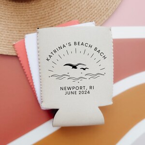 K&ouml;nnte beinhalten: Beigefarbener Getr&auml;nkedosenk&uuml;hler mit schwarzem Text und Grafik. Der Text lautet "Katrina's Beach Bach, Newport, RI, June 2024". Die Grafik zeigt eine stilisierte Sonne mit V&ouml;geln, die &uuml;ber Wellen fliegen.