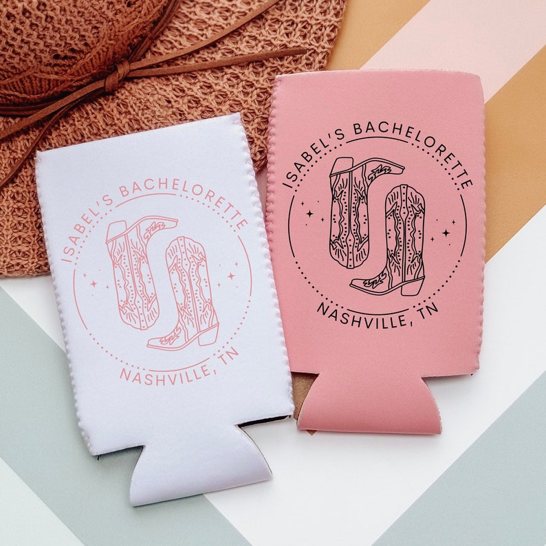 May include: Two white and pink can coolers with a black and white design of cowboy boots. The text on the coolers reads "Isabel's Bachelorette Nashville, TN".