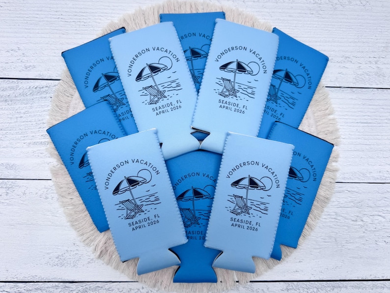 Puede incluir: Un conjunto de enfriadores de latas azules y celeste. Cada enfriador presenta una escena de playa con una sombrilla, una silla y el texto "Vonderson Vacation, Seaside, FL, April 2026".