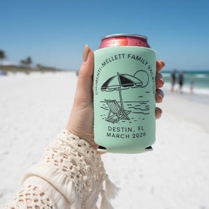 Puede incluir: Un enfriador de latas verde claro con un dise&ntilde;o de playa en blanco y negro, que incluye una sombrilla y una silla. El texto dice "CHIMENTI-MELLETT FAMILY VACATION DESTIN, FL MARCH 2026". El enfriador se sostiene en una playa soleada.