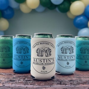 May include: A collection of beer can coolers in various colors, including gray, green, blue, and white. Each cooler features the text "BREWS BEFORE I DO" and "AUSTIN'S BACHELOR WEEKEND 2026" with a beer mug graphic. The background includes balloons.
