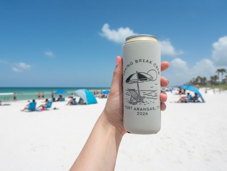 Puede incluir: Un enfriador de latas gris claro con el texto "Spring Break Crew Port Aransas, TX 2026" y un gr&aacute;fico de escena de playa. El enfriador se sostiene contra un fondo de playa soleado con gente y sombrillas.