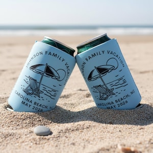 Puede incluir: Dos enfriadores de latas azul claro con dise&ntilde;o de playa, que incluyen una sombrilla, una silla de playa y el texto "JOHNSON FAMILY VACATION CAROLINA BEACH, NC MAY 2026." Est&aacute;n en la arena de una playa.