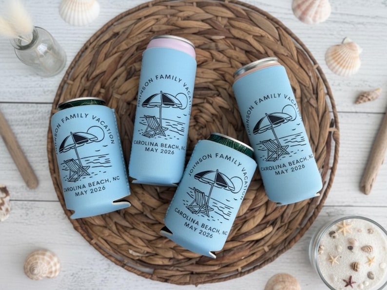 Puede incluir: Cuatro enfriadores de latas azul claro con un dise&ntilde;o de playa. Cada enfriador presenta una ilustraci&oacute;n en blanco y negro de una sombrilla, una silla y el texto "JOHNSON FAMILY VACATION CAROLINA BEACH, NC MAY 2026". Los enfriadores est&aacute;n colocados sobre una estera tejida con conchas marinas.