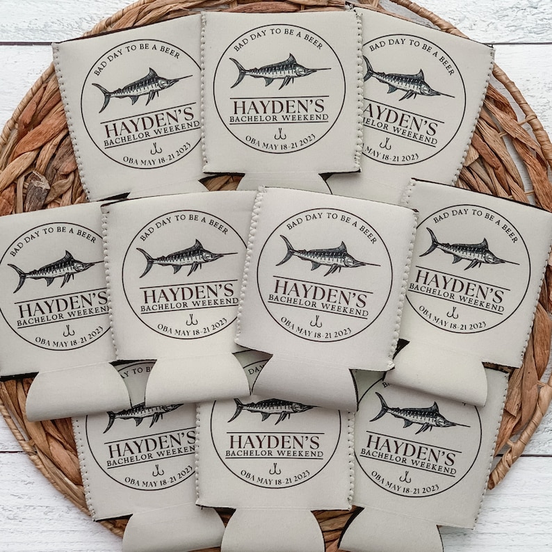 May include: A set of eight beige can coolers with a black marlin fish graphic and the text "Hayden's Bachelor Weekend" with a fishing hook symbol and the date "OBA May 18-21 2023".