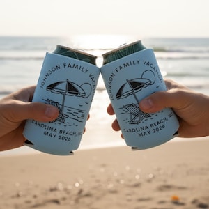 Puede incluir: Dos enfriadores de latas azul claro con un gr&aacute;fico de escena de playa, levantados en un brindis en una playa. Los enfriadores tienen el texto "JOHNSON FAMILY VACATION CAROLINA BEACH, NC MAY 2026".