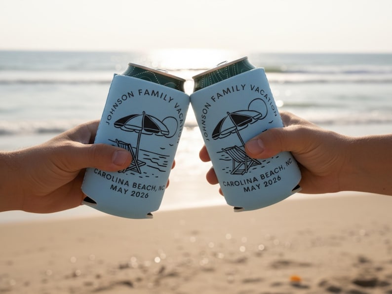 Puede incluir: Dos enfriadores de latas azul claro con un gr&aacute;fico de escena de playa, levantados en un brindis en una playa. Los enfriadores tienen el texto "JOHNSON FAMILY VACATION CAROLINA BEACH, NC MAY 2026".