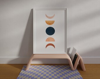 May include: A framed print with a minimalist design featuring five abstract moons in shades of brown, orange, and blue against a white background. The print is displayed on a pink shelf with a checkered rug underneath.