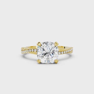 May include: A gold engagement ring with a large, square-cut diamond center stone. The band features a twisted design with smaller diamonds set along the sides. The ring is set against a white background.