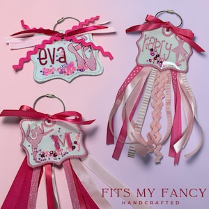 May include: Three personalized ballet-themed keychains with pink and white ribbons. Each keychain features a name, ballet shoes, or a ballerina silhouette, with decorative sequins. The text "Fits My Fancy Handcrafted" is at the bottom.
