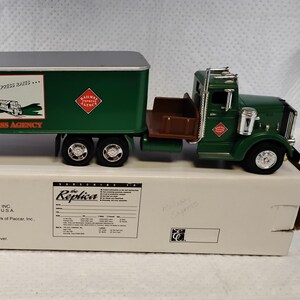 May include: A green Ertl Collectibles toy semi-truck with a trailer featuring the Railway Express Agency logo and text. The truck sits on its original white cardboard box, which displays stock number F514 and 1995 Ertl Company branding.