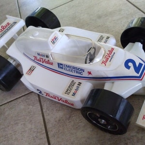K&ouml;nnte beinhalten: Ein wei&szlig;es Spielzeug-Rennwagen mit schwarzen R&auml;dern und rot-wei&szlig;-blauen Aufklebern. Das Auto tr&auml;gt die Aufschriften "True Value", "Mobil" und "Emerson Electric". Das Auto ist mit der Nummer "2" versehen.