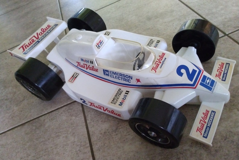 K&ouml;nnte beinhalten: Ein wei&szlig;es Spielzeug-Rennwagen mit schwarzen R&auml;dern und rot-wei&szlig;-blauen Aufklebern. Das Auto tr&auml;gt die Aufschriften "True Value", "Mobil" und "Emerson Electric". Das Auto ist mit der Nummer "2" versehen.
