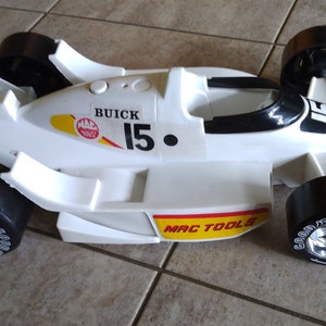 K&ouml;nnte beinhalten: Wei&szlig;es Spielzeug-Rennwagen mit schwarzen Reifen und einem roten und gelben MAC TOOLS-Logo. Das Auto hat einen schwarzen Spoiler und die Nummer 15 an der Seite. Das Auto ist ein Buick.