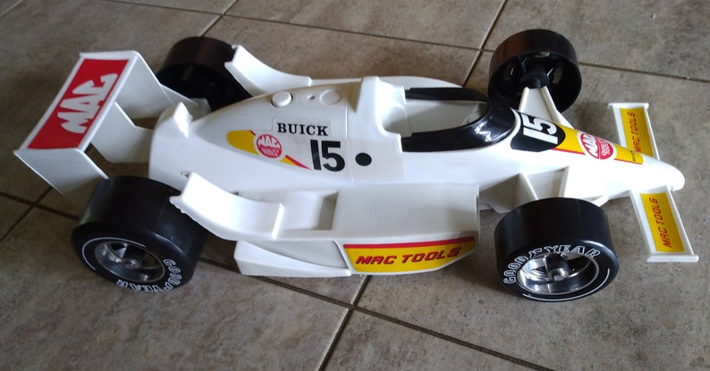 K&ouml;nnte beinhalten: Wei&szlig;es Spielzeug-Rennwagen mit schwarzen Reifen und einem roten und gelben MAC TOOLS-Logo. Das Auto hat einen schwarzen Spoiler und die Nummer 15 an der Seite. Das Auto ist ein Buick.