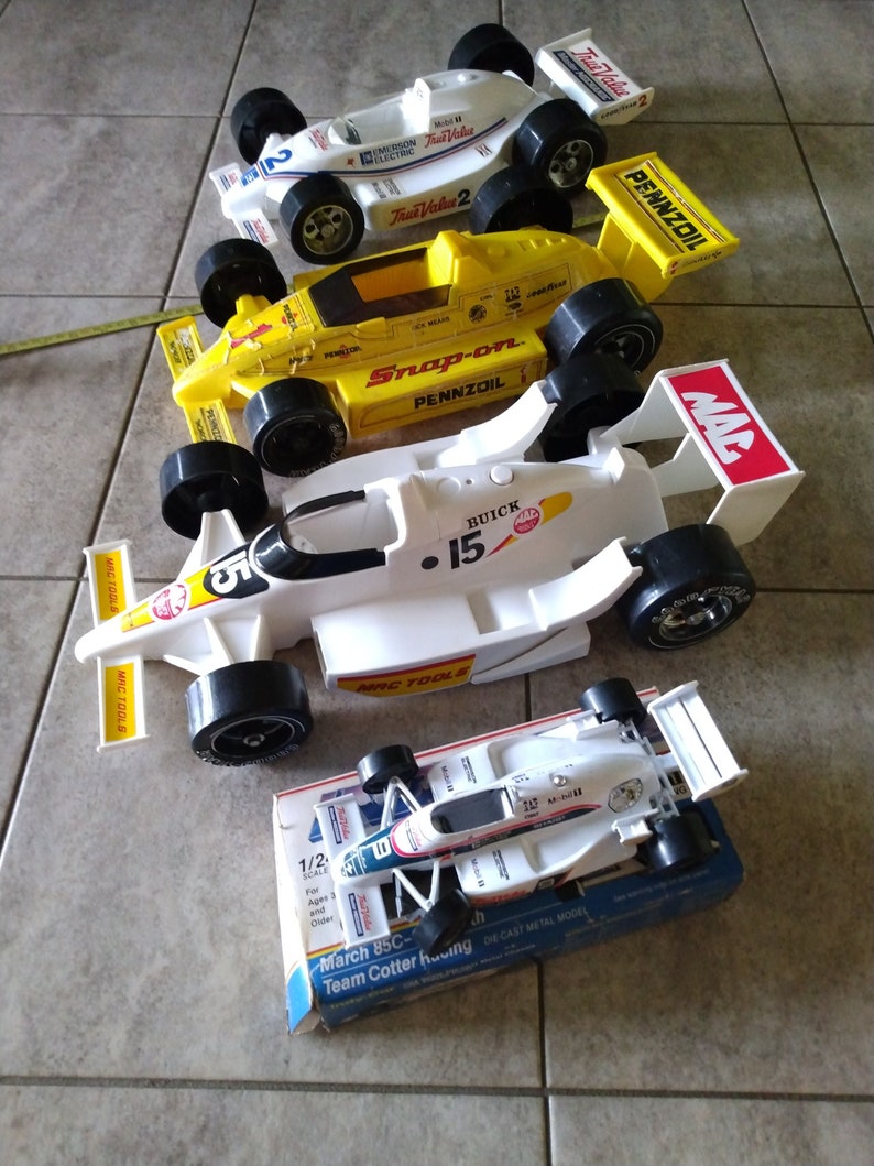 K&ouml;nnte beinhalten: Eine Sammlung von f&uuml;nf Spielzeug-Rennwagen, darunter ein wei&szlig;es Auto mit den Aufdrucken "MAC TOOLS" und "BUICK 15", ein gelbes Auto mit den Aufdrucken "Snap-on" und "PENNZOIL" und ein wei&szlig;es Auto mit dem Aufdruck "True Value 2". Die Autos sind alle im Ma&szlig;stab 1:2 und aus Metallguss gefertigt.