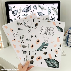 May include: Three white binders with a tropical leaf and abstract pattern. The front binder says "Guided Reading" with the text "Year 2J 2020".
