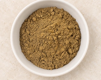 Puede incluir: Un cuenco de cerámica blanca lleno de un polvo fino de color marrón terroso. La sustancia tiene una textura granular y está distribuida uniformemente dentro del recipiente circular, mostrando un color marrón oliva apagado y constante.