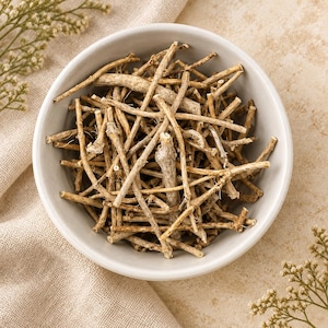 Può includere: Una ciotola rotonda in ceramica grigio chiaro riempita con una collezione di sottili ramoscelli o radici legnose essiccate di colore marrone chiaro. I pezzi sono tagliati in lunghezze corte e irregolari con una superficie ruvida e strutturata.